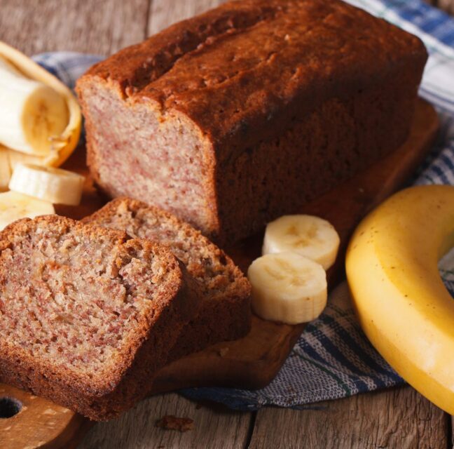 Sliced loaf of banana bread on a wooden board with fresh bananas