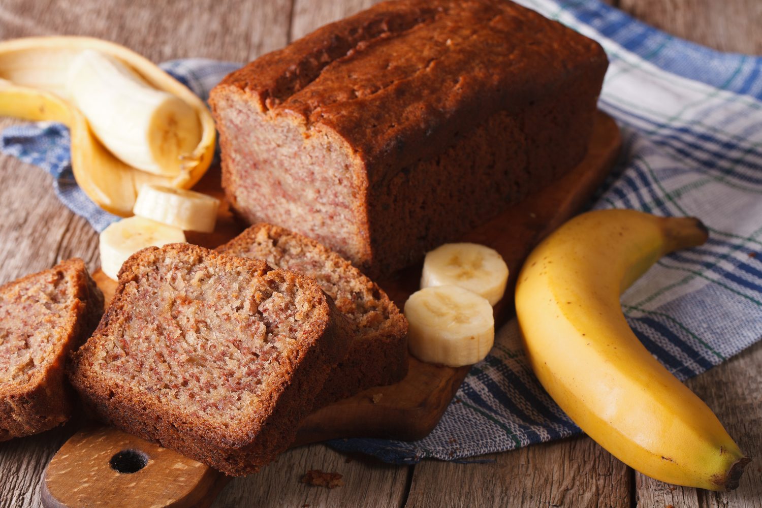 Sliced loaf of banana bread on a wooden board with fresh bananas